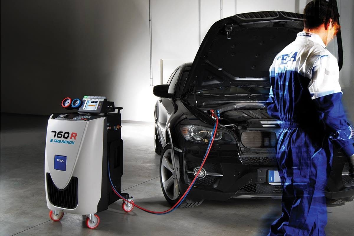 Technicien branchant une station de recharge de climatisation sur une voiture capot ouvert
